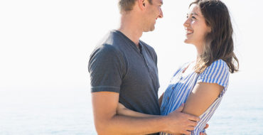 A woman who listened to these dating tips smiling up at her boyfriend on the beach.