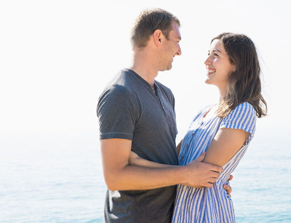 A woman who listened to these dating tips smiling up at her boyfriend on the beach.