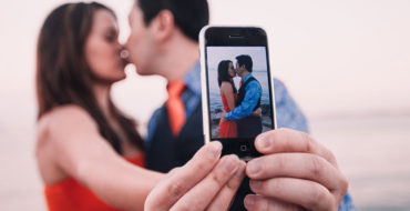 A couple taking a selfie while kissing, displaying an example of what social media and relationships.