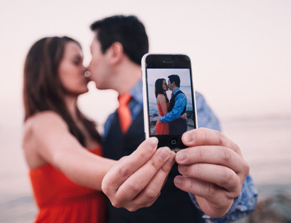 A couple taking a selfie while kissing, displaying an example of what social media and relationships.