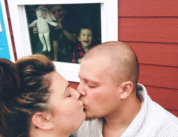 A woman who's a single parent and dating, kissing her date while her kids are inside pushing their faces against the window and making funny faces.