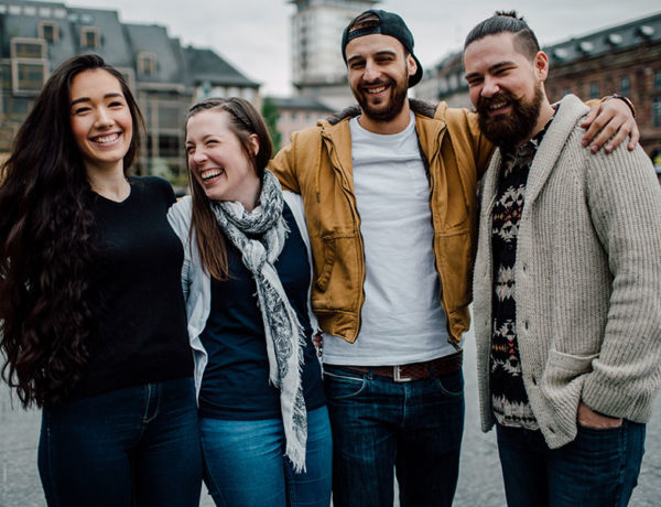 A group of men and women who learned how to make friends in a new city, hugging and laughing with each other as they hang out.