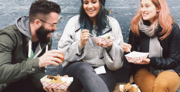 A group who learned how to find friends online laughing and eating together outside.