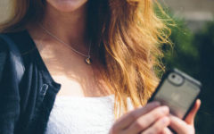 A woman who's trying to avoid text flirting mistakes, laughing while outside on her phone typing.