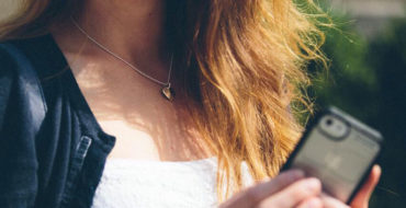 A woman who's trying to avoid text flirting mistakes, laughing while outside on her phone typing.