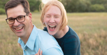 A man over 40 who's never been in a relationship before, laughing with his girlfriend in a field as he learns how to navigate his way through it.