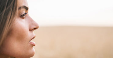 A woman who's battling with codependency standing in a field thinking.