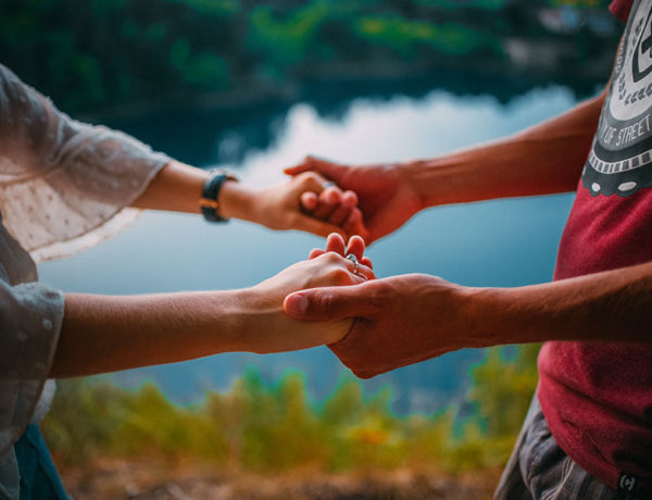 A woman who's wondering, "Why do you love me?" holding hands by a lake with her partner who's telling her just that.