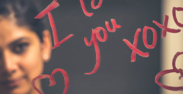 A woman writing, "I love you" on a mirror with lipstick, one of the romantic gestures for him that guys appreciate.