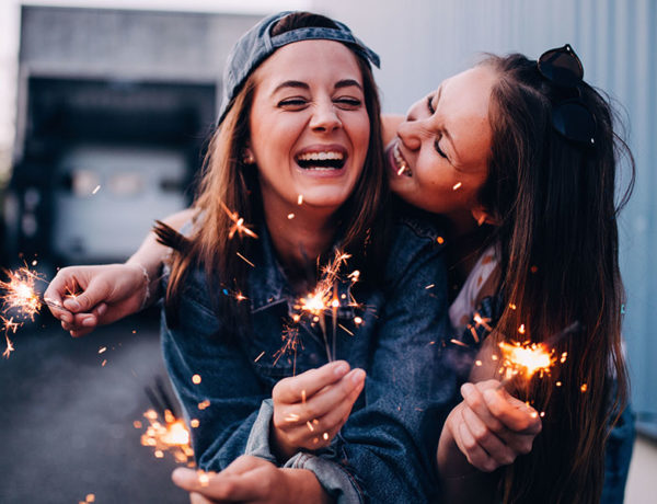 Two BFFs who share friendship signs laughing while playing wish sparklers.