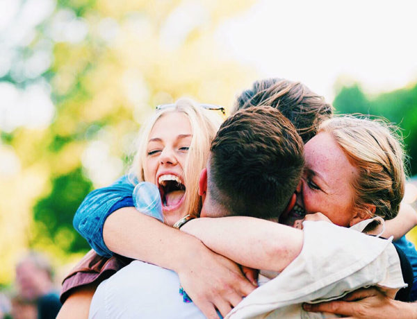 A group of loyal friends laughing and hugging each other outside.