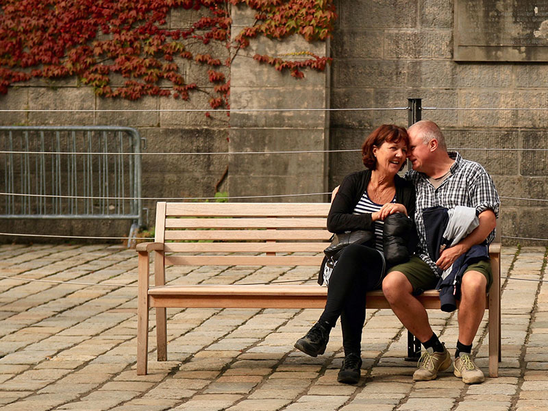 A couple who met on a 50 and over dating site, sitting on a bench and cuddling a little in the sun.