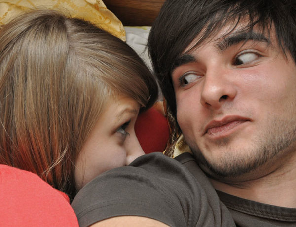 A girl wondering how to make a man want you, looking at the guy she's seeing while in bed.