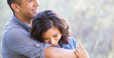 A man who is a jealous boyfriend hugging his girlfriend tight as they laugh together.