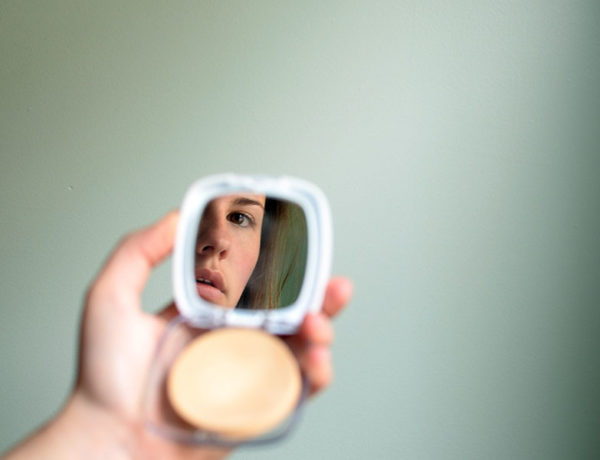 A woman who has body image issues, looking at her reflection in the mirror of her makeup compact.