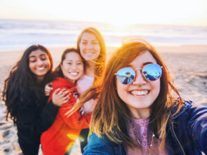 Un groupe de filles qui se sont rencontrées sur l'application Tinder for friends, à la plage, souriant en prenant une photo.