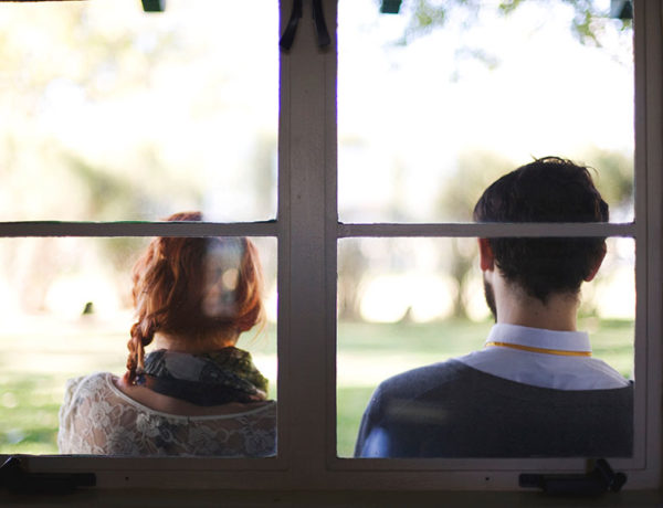A man who has a fear of commitment sitting outside leaning against a window with her girlfriend as they have a discussion.