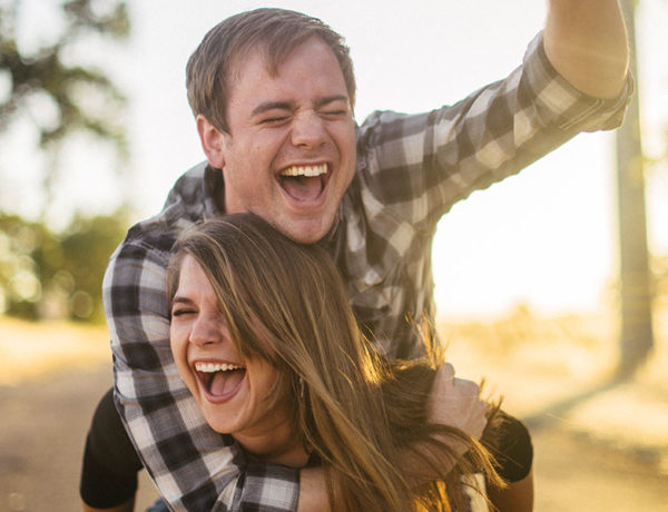 A couple who learned how to be friends with your ex, laughing in the sun while the woman gives the man a piggyback ride.