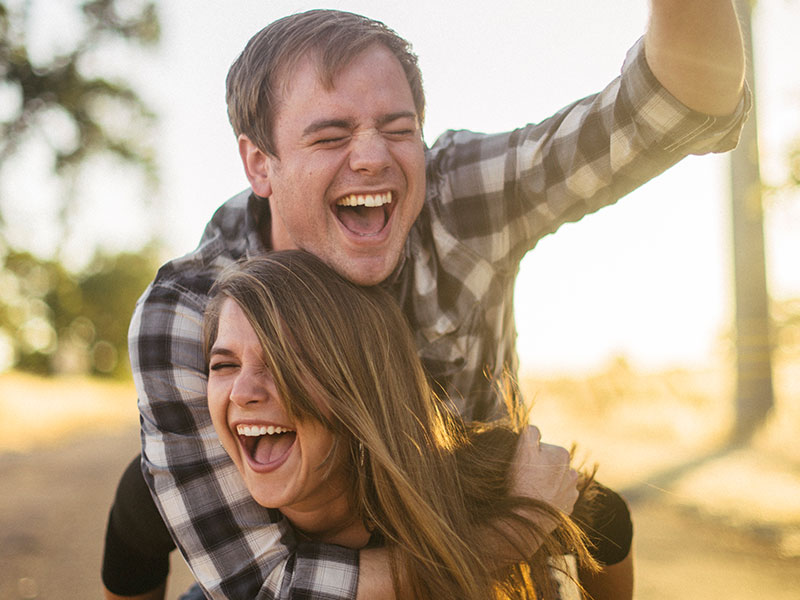 A couple who learned how to be friends with your ex, laughing in the sun while the woman gives the man a piggyback ride.