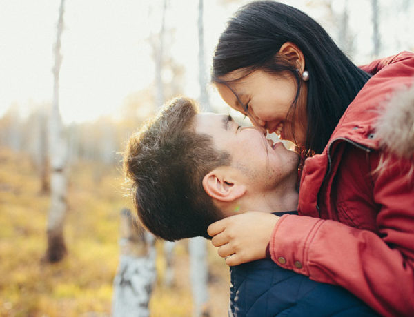 A couple who's best friends with each other smiling and laughing as they kiss in the woods.