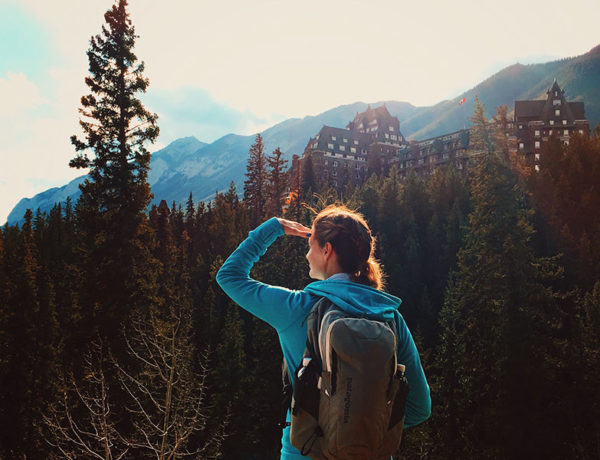 A woman who's surviving infidelity, hiking in the woods and looking towards the sun.