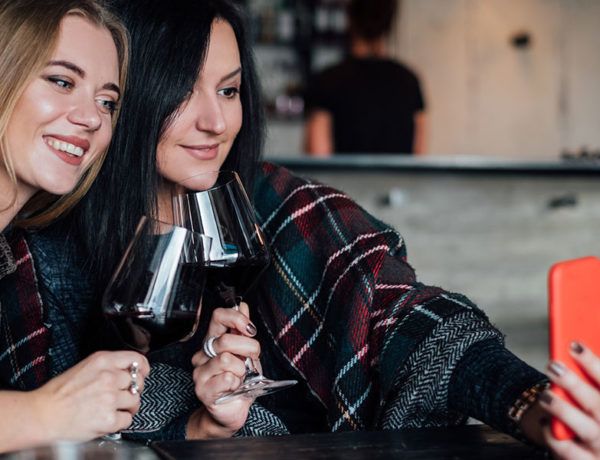 Two women who are bad friends smiling and taking a selfie together with wine.