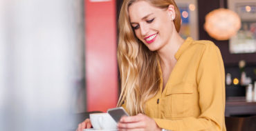 A woman on an online dating app at a coffee shop, smiling while on her phone.
