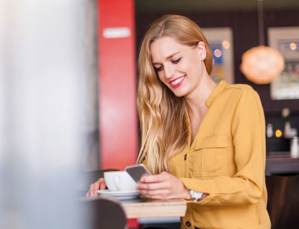 A woman on an online dating app at a coffee shop, smiling while on her phone.