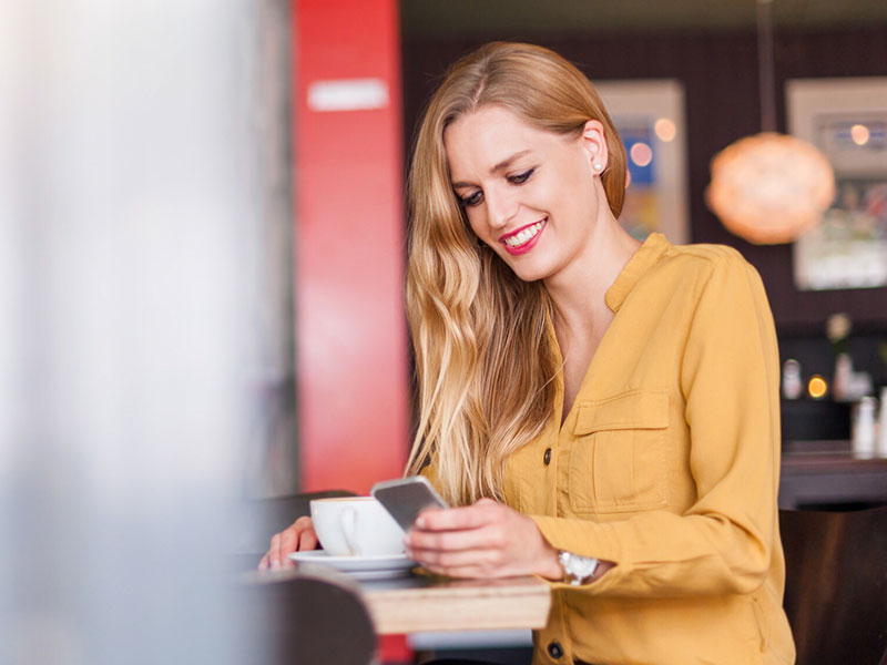 A woman on an online dating app at a coffee shop, smiling while on her phone.