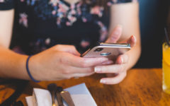 A woman who took these dating profile tips, at a restaurant looking through dating profiles on her phone.