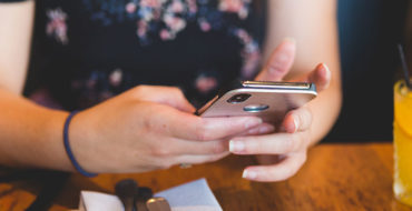 A woman who took these dating profile tips, at a restaurant looking through dating profiles on her phone.