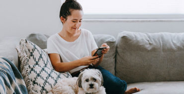 A woman who listened to these online dating first message tips smiling and texting while on the couch with her dog.