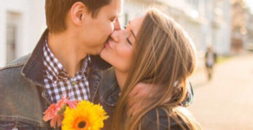 A guy who learned how to woo someone, kissing his girlfriend while holding flowers.